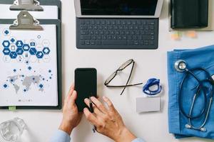 top view of smart medical doctor working with mobile phone and laptop computer and stethoscope on dark wooden desk photo