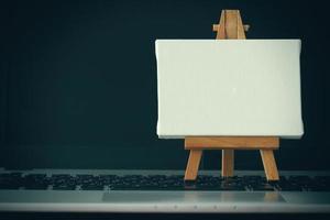 blank canvas and wooden easel on laptop computer as concept photo