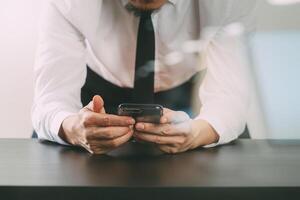 close up of businessman working with smart phone on wooden desk in modern office with virtual icon diagram with glass reflected view photo