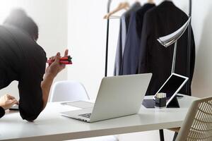 Fashion designer working with mobile phone and using laptop with digital tablet computer in modern studio photo