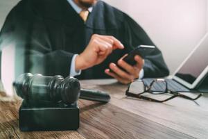 concepto de justicia y derecho. juez masculino en una sala de audiencias con el mazo, trabajando con un teléfono inteligente, teclado de acoplamiento de tableta digital en una mesa de madera, efecto de filtro foto