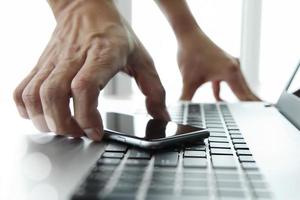 Businessman hand using laptop and mobile phone in office photo