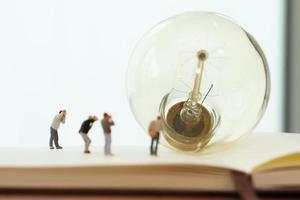 Creative idea concept - miniature photographer with vintage light bulb on open paper notebook photo