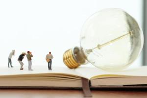 Creative idea concept - miniature photographer with vintage light bulb on open paper notebook photo