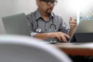 smart medical doctor hand working with smart phone,digital tablet computer,stethoscope eyeglass,on wood desk photo