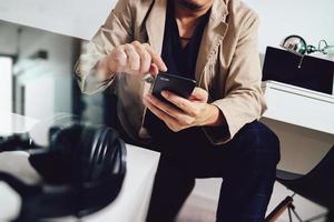 young man is sitting on a sofa shopping on line is listening music with headphones is holding smart phone on his hand at home,omni channel concept photo