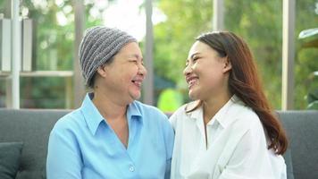 mujer paciente con cáncer con pañuelo en la cabeza sonriendo con su hija solidaria en el concepto de hogar, salud y seguro.