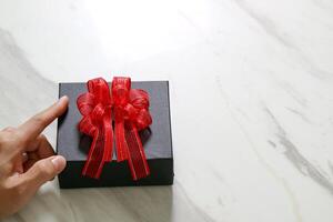 gift giving,man hand holding a gift box in a gesture of giving on white gray marble table background photo