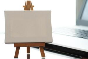 blank canvas and wooden easel on laptop computer as concept photo