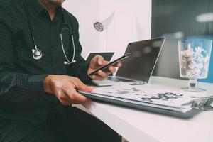 smart medical doctor working with smart phone and digital tablet and laptop computer and stethoscope on wood desk in modern office photo