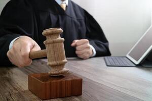 justice and law concept.Male judge in a courtroom striking the gavel,working with digital tablet computer docking keyboard on wood table photo