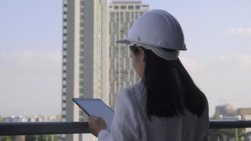 vrouwelijke bouwingenieur met een tabletcomputer op een bouwplaats. zelfverzekerde vrouw architect in witte helm kijken naar een bouwplaats. bouw- en architectuurconcept. video