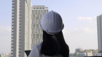 ingegnere edile femminile con un tablet PC in un cantiere edile. architetto donna sicura in casco bianco guardando un cantiere. concetto di costruzione e architettura. video