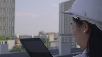 weiblicher Bauingenieur mit einem Tablet-Computer auf einer Baustelle. Selbstbewusste Architektin mit weißem Helm, die auf eine Baustelle blickt. Bau- und Architekturkonzept. video