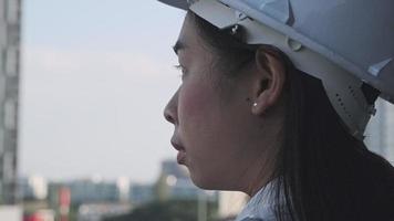 Female construction engineer with a tablet computer at a construction site. Confident woman architect in white helmet looking at a construction site. Construction and architecture concept. video