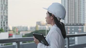 uma arquiteta confiante de chapéu branco olha para a câmera com um sorriso. engenheira de construção feminina com um computador tablet em um canteiro de obras. video