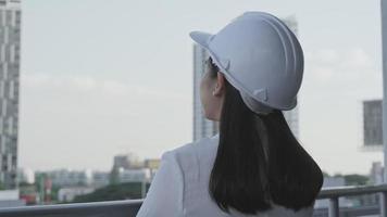 Female construction engineer with a tablet computer at a construction site. Confident woman architect in white helmet looking at a construction site. Construction and architecture concept. video