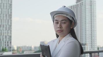 engenheira de construção feminina com um computador tablet em um canteiro de obras. arquiteto de mulher confiante no capacete branco, olhando para um canteiro de obras. conceito de construção e arquitetura. video