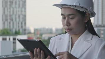 Female construction engineer with a tablet computer at a construction site. Confident woman architect in white helmet looking at a construction site. Construction and architecture concept. video