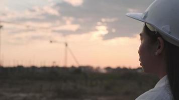 weiblicher Bauingenieur mit einem Tablet-Computer auf einer Baustelle bei Sonnenuntergang. Selbstbewusste Architektin mit weißem Helm, die auf eine Baustelle blickt. video