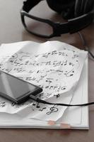 Closeup of smartphone with headphone on musical notes paper on wooden desk photo