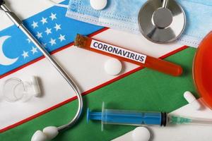 Coronavirus, nCoV concept. Top view protective breathing mask, stethoscope, syringe, pills on the flag of Uzbekistan. photo