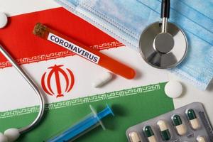 Coronavirus, nCoV concept. Top view of a protective breathing mask, stethoscope, syringe, pills on the flag of Iran. photo