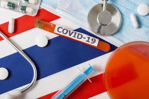 Coronavirus, the concept COVid-19. Top view protective breathing mask, stethoscope, syringe, pills on the flag of Thailand. photo