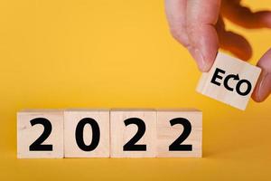 A hand holds wooden cubic blocks on a yellow background of 2022. The ecological year is 2022. photo
