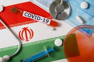 Coronavirus, the concept COVid-19. Top view of a protective breathing mask, stethoscope, syringe, pills on the flag of Iran. photo
