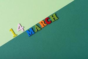 14 de marzo, diseño de portada de fecha con letras k de madera multicolores sobre un fondo de papel verde. foto