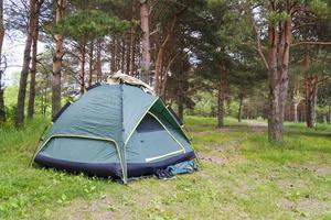 Green tent in the summer, pine forest, sneakers near the tent. photo