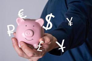 An unrecognizable businessman holding a sparkling pink piggy bank with currency icons from around the world. photo