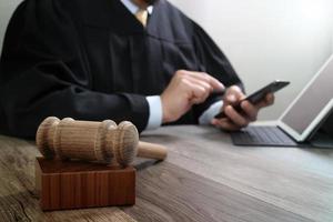 justice and law concept.Male judge in a courtroom with the gavel,working with smart phone,digital tablet computer docking keyboard on wood table photo