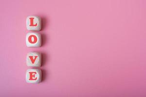 The word love is in the shape of a heart on wooden cubes on a pink background. photo