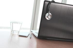 laptop computer and stethoscope and smart phone in medical workspace office and glass of water as concept photo