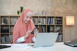 Beautiful businesswoman who Islamic female person is talking on her mobile phone communication and happy smiling because internet online order in laptop, modern lifestyle, e-commerce occupation. photo