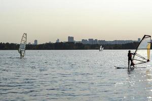 Windsurfer. Man is surfing on the background of skyscrapers. Man on a windsurf board. Windsurfing in the city. Water sports. Surfing with a sail. Windsurfing equipment. Active lifestyle. photo