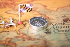 Maryland flag, airplane and compass on an old world map. photo