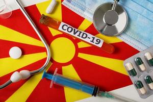 Coronavirus, the concept COVid-19. Top view protective breathing mask, stethoscope, syringe, pills on the flag of North Macedonia. photo