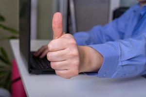 A businessman gives a thumbs up while sitting at his laptop. photo