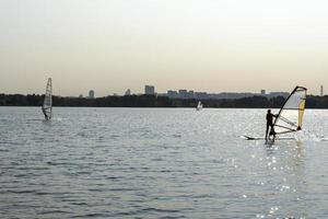 Windsurfer. Man is surfing on the background of skyscrapers. Man on a windsurf board. Windsurfing in the city. Water sports. Surfing with a sail. Windsurfing equipment. Active lifestyle. photo