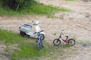 An old, vintage moped and two bicycles stand on the sand. photo