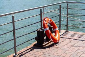 A lifebuoy hangs on the railing and casts a shadow on the stone pier. photo