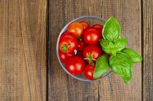 Red ripe cherry tomatoes, green basil in glass. Studio Photo