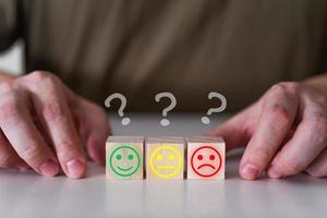 Smiling, indifferent and sad emoticons on wooden cubes under a question mark. photo