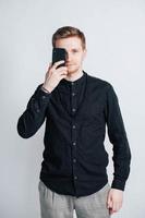 Young man in a black shirt with a smartphone in his hands on a white background. Copy, empty space for text photo