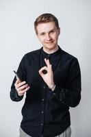 Young man in a black shirt with a smartphone in his hands on a white background. Copy, empty space for text photo