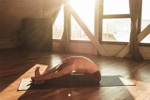 Man with a naked torso practicing yoga training in studio in front of a window. Copy, empty space for text photo
