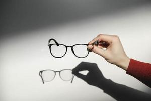 Black optical glasses in man's hand making a shadow on white background. Copy, empty space for text photo